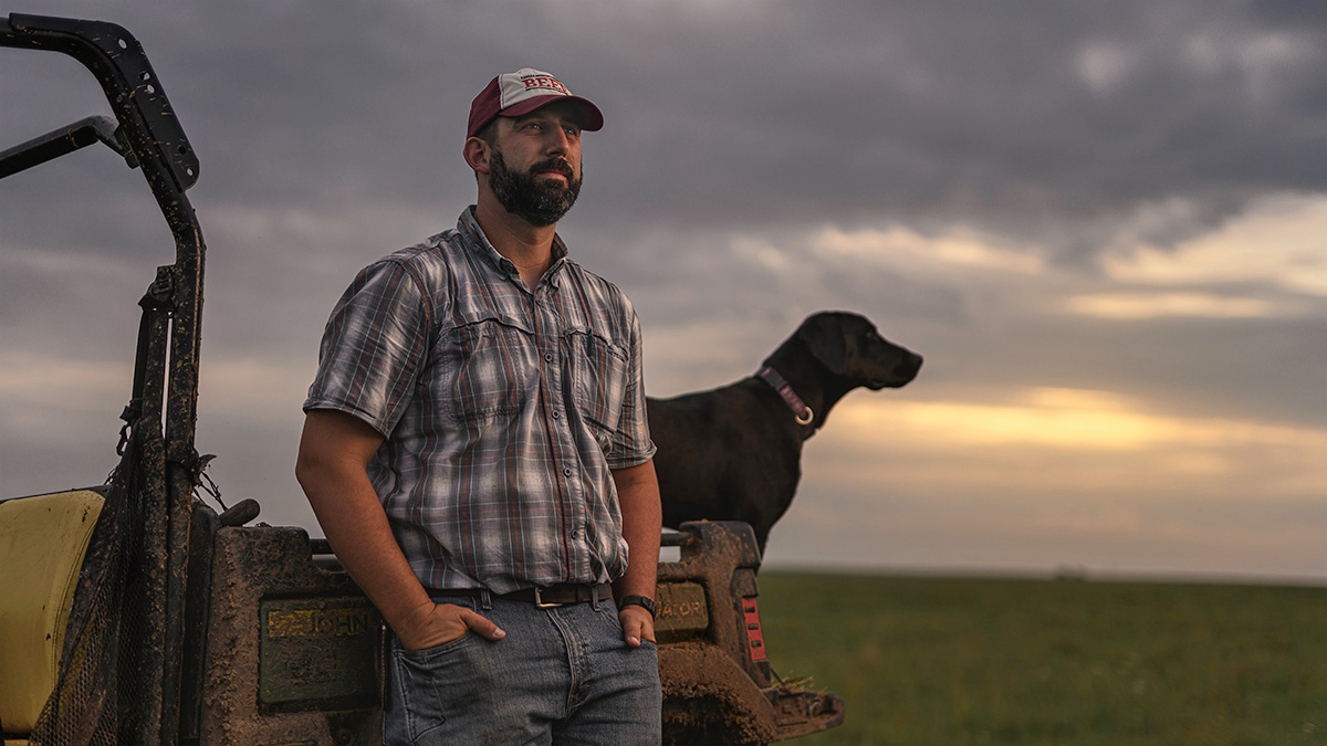 rancher with black lab mix on pasture john deere gator